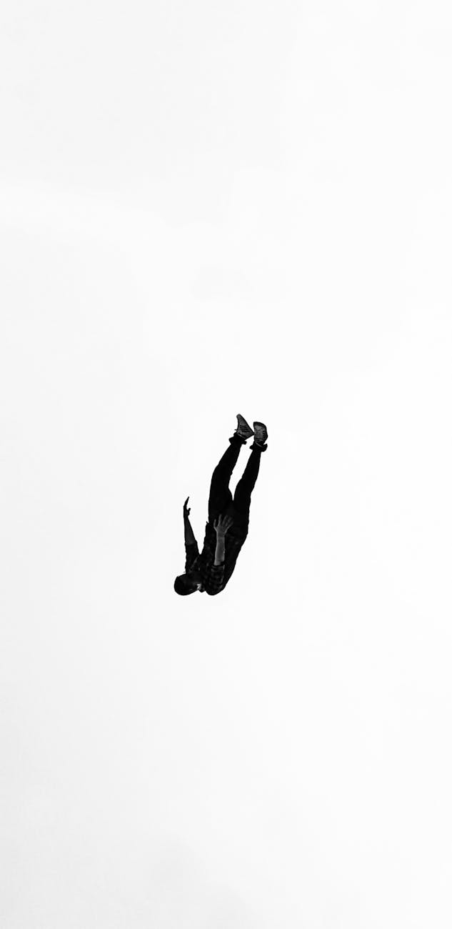 A dramatic silhouette of a man falling upside down against a white background, creating a minimalist abstract visual.