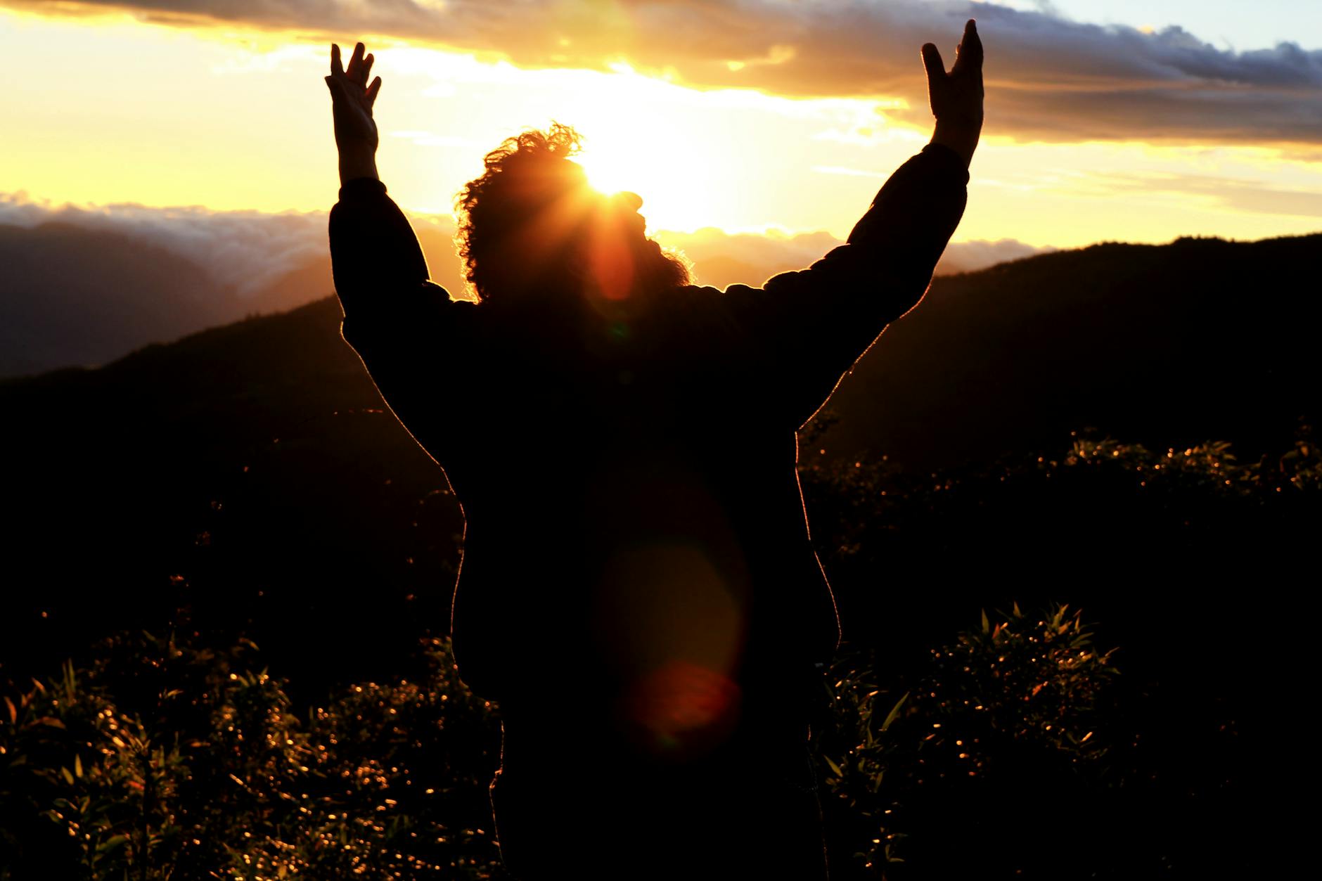 A silhouette of a man with arms raised against a stunning sunset in the mountains of Loja, Ecuador.