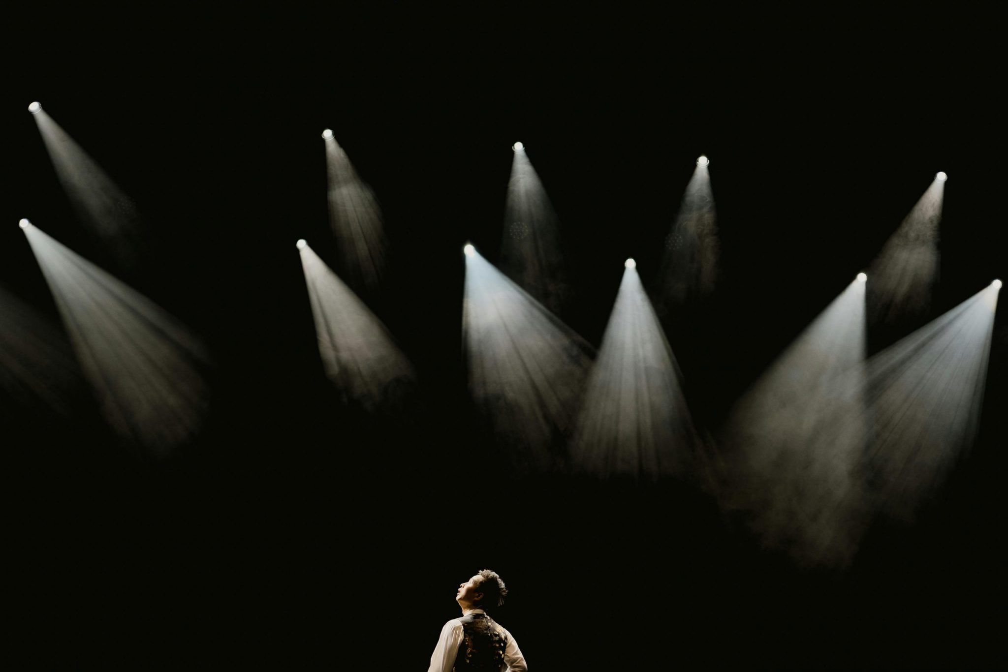 A solo performer stands in a spotlight on a dark stage during a dramatic moment.