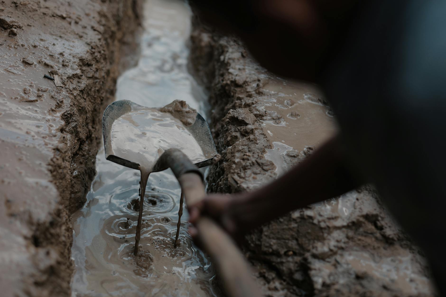 A child digs with a spade in a muddy trench in Gaza, showcasing resilience and everyday life.