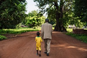 A father and son walking together on a peaceful rural dirt road surrounded by trees.