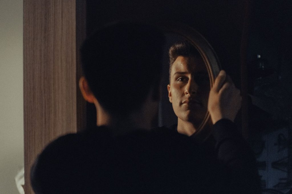 A man gazing at his reflection, capturing an introspective moment indoors.