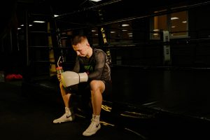 Young male boxer sitting in the ring holding gloves and a water bottle, taking a break.