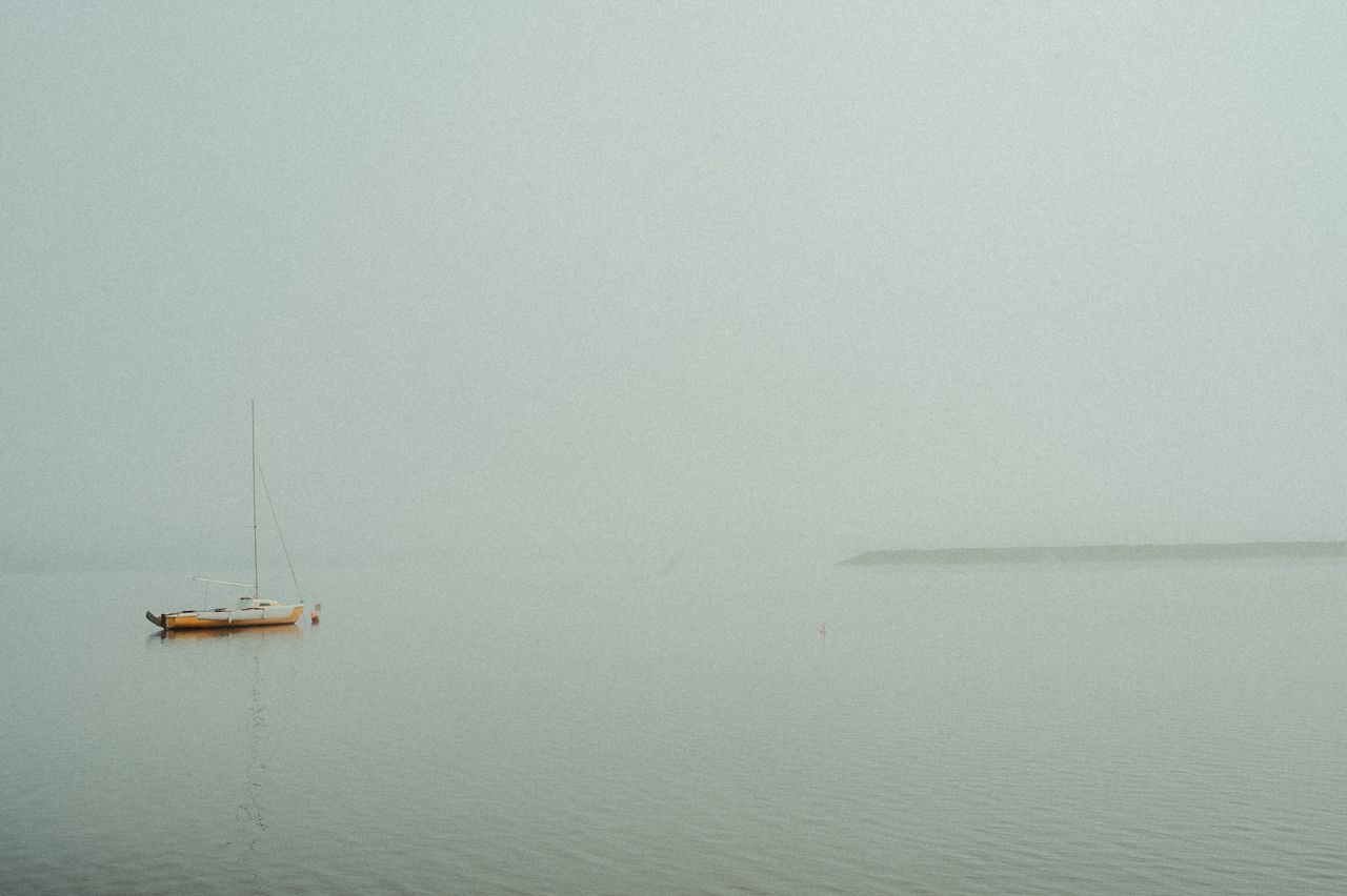 Calm sailboat floating on the ocean during a misty morning, creating a peaceful ambiance.